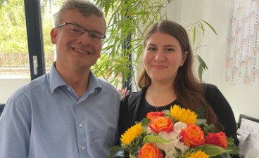 bfz Mitarbeiterin Sandra Seel hält einen Blumenstrauß in der Hand, neben ihr Koordinator Jörn Fleischer.