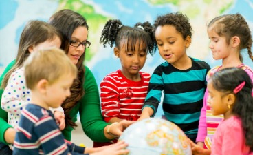 Eine Schulbegleiterin zeigt Kindern verschiedener Herkunft die Lage der Herkunftsländer auf einem Globus.