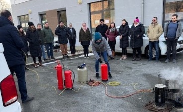 eine Personengruppe schaut einer Frau beim Bedienen eines Feuerlöschers zu