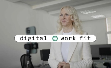 Digital work fit: Eine Frau in weißem Blazer steht vor der Kamera eines Smartphones und lächelt selbstbewusst.