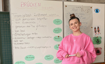 News- Bild: Eine Frau posiert vor einem Whiteboard, auf welchem ein Tafelbild zu sehen ist