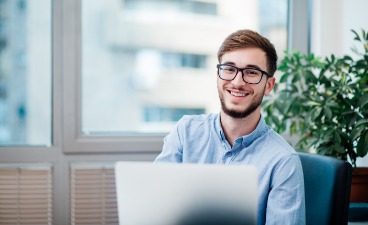 News- Bild: Ein Mann posiert vor einem Laptop sitzend