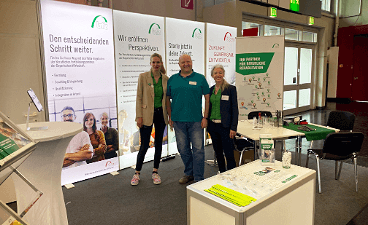 News- Bild: Ein Mann und zwei Frauen posieren vor einem Messestand stehend