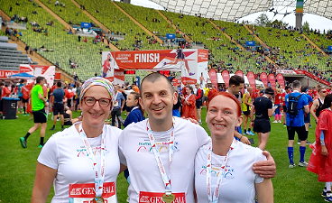 News- Foto: Ein Mann und zwei Frauen posieren in einem Stadion nebeneinander stehend