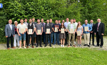 News- Foto: Viele Personen posieren auf einer Wiese nebeneinander stehend mit einem Zeugnis in der Hand