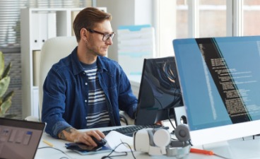  Ein junger Mann sitzt aufmerksam vor einem Computer an einem  Schreibtisch