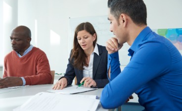 Die Lehrerin erklärt zwei Teilnehmern am Schreibtisch die Inhalte des Unterrichts