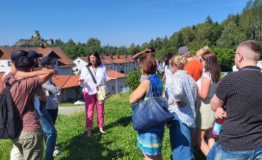 Newsbild: Mehrere Personen stehen auf einer Wiese und hören einer Frau zu, die einen Vortrag hält.