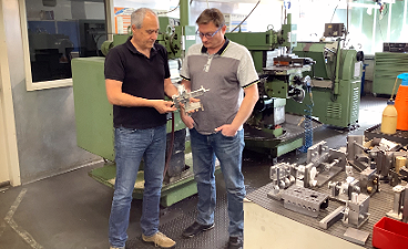 News- Foto: Zwei Männer posieren vor einer Maschine stehend in einer Werkstatt